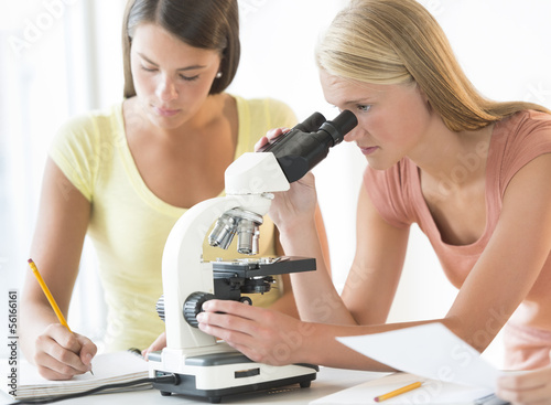 Student Using Microscope With Friend Making Notes