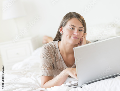 Girl Smiling While Using Laptop In Bed