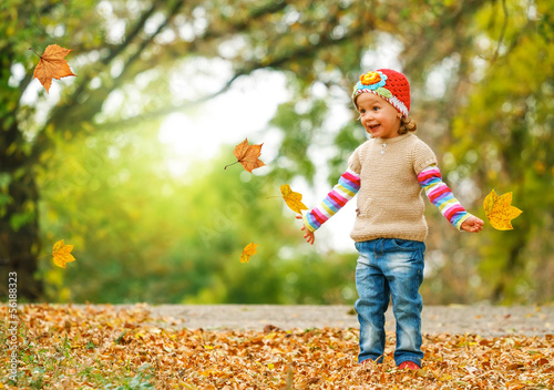 Cute child playing with autumn leaves