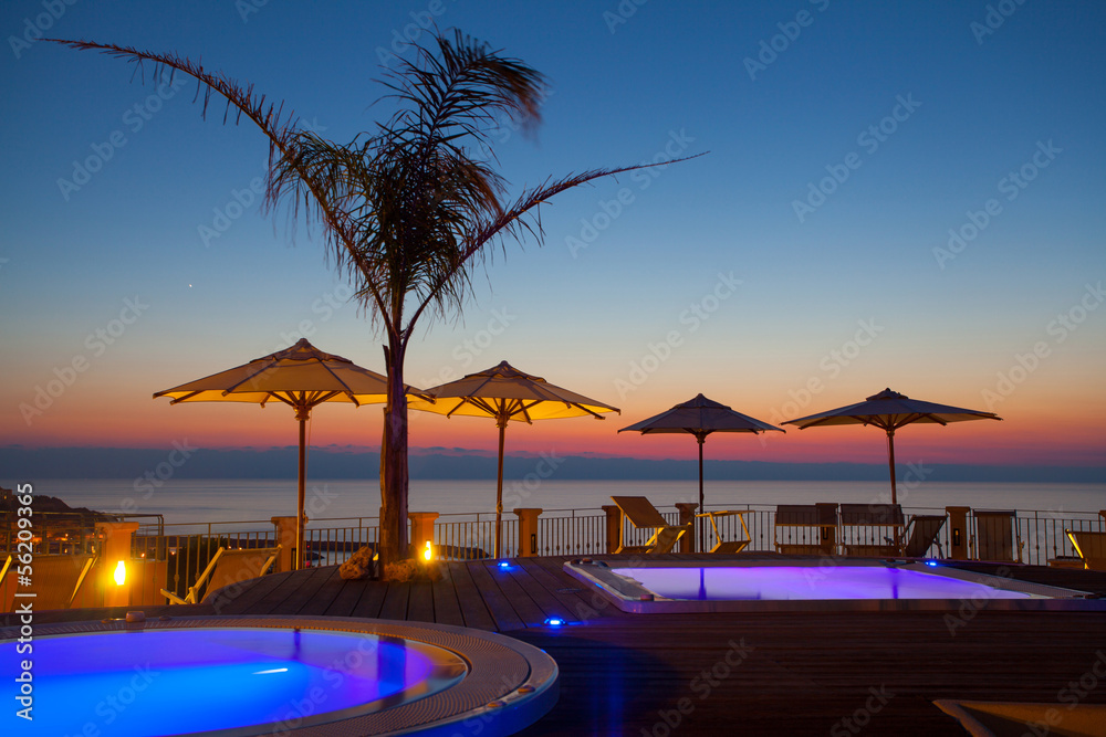 Summer time: beautiful dawn at pool area with palm and parasols,