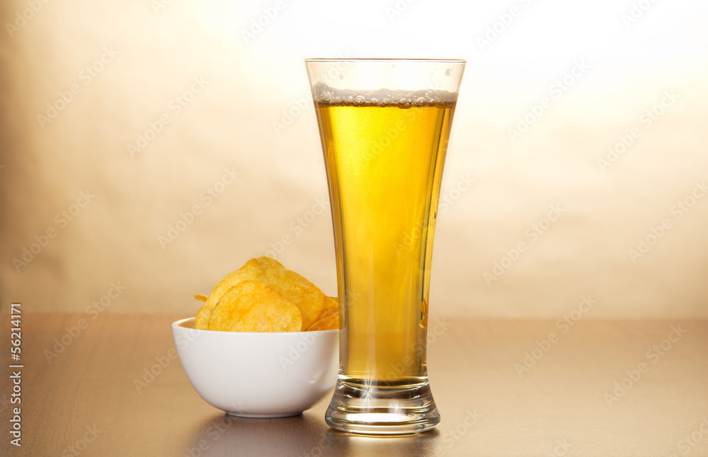 Glass of light beer and bowl with chips against paper Glass of light beer and bowl with chips against paper