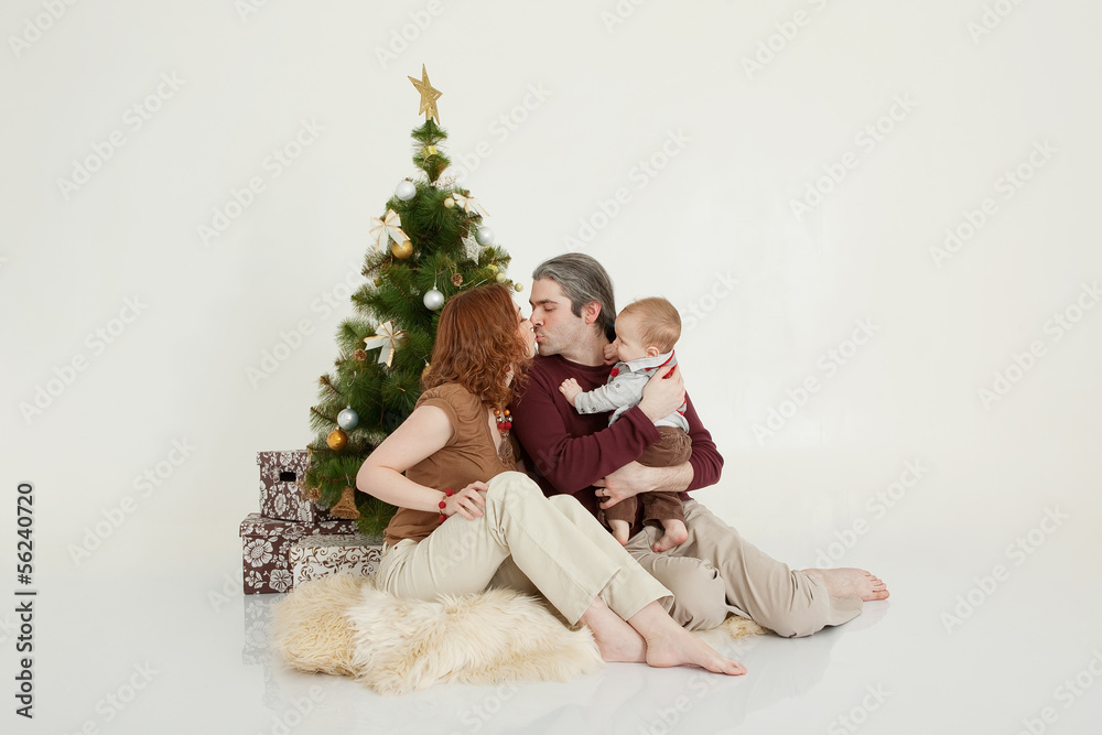 Happy family sitting at the new-year tree on white studio Happy family sitting at the new-year tree on white studio