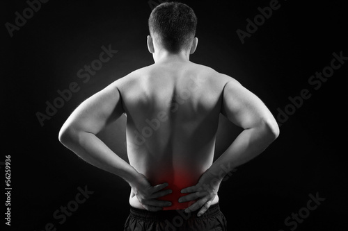Young man with back pain, on black background