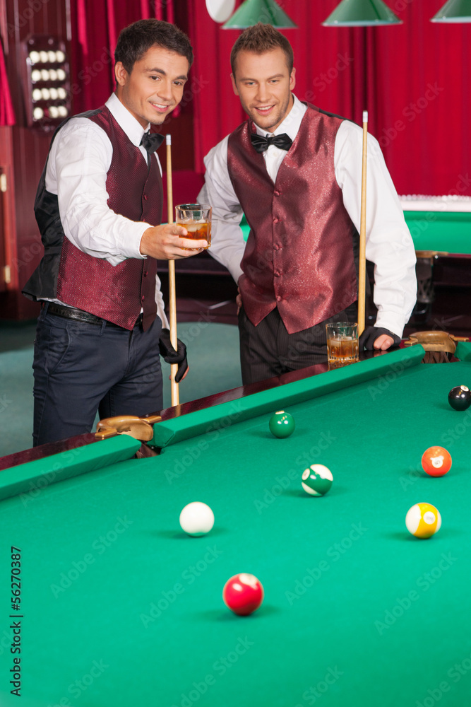 Fototapeta premium Pool game. Two cheerful young men playing pool and drinking