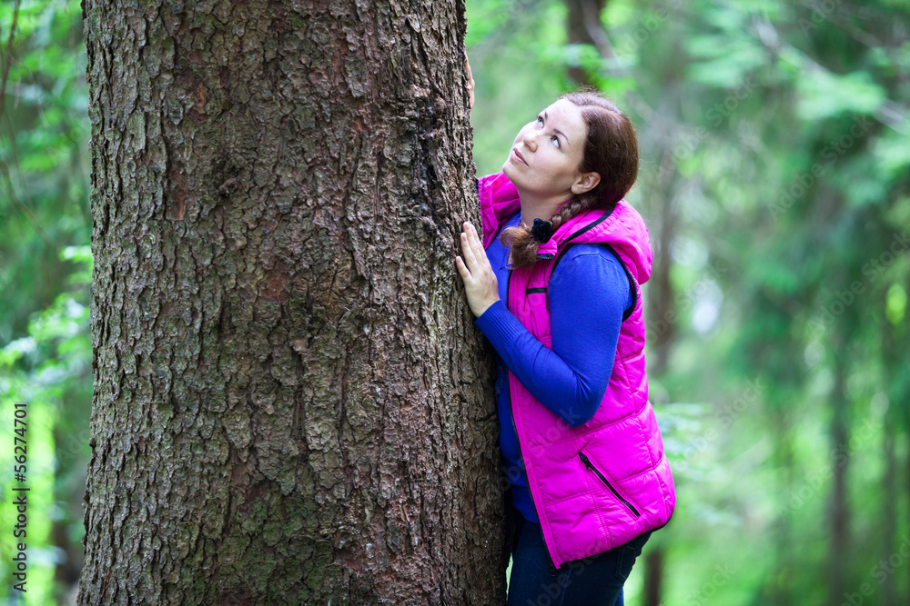 Cute Caucasian girl hugging a big pine tree trunk in the forest Cute Caucasian girl hugging a big pine tree trunk in the forest