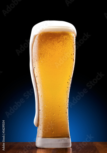 Szklanka jasnego piwa z pianą i bąbelkami na drewnianym blacie © rafciu1988