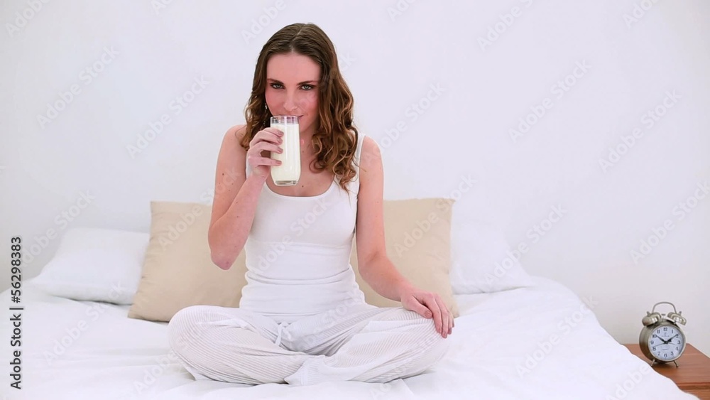 Pretty model sitting on bed drinking glass of milk Pretty model sitting on bed drinking glass of milk