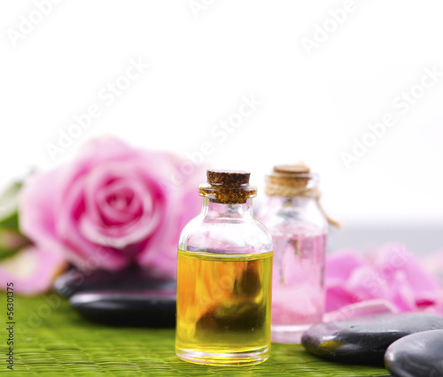 Pink roses with petals and massage oil with stone on mat