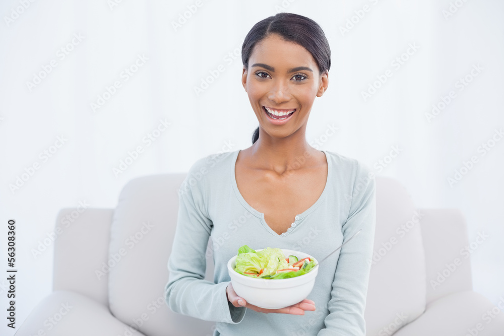 Smiling attractive woman sitting on cosy sofa holding salad