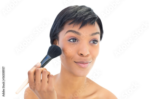 Content black haired woman applying powder on her cheeks