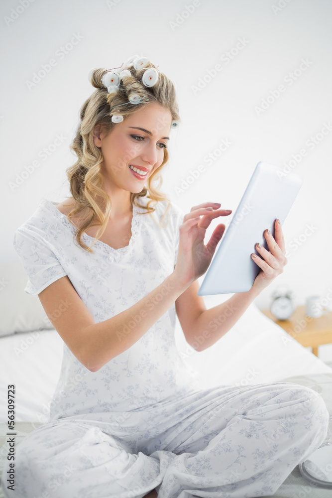Happy blonde wearing hair curlers using tablet Happy blonde wearing hair curlers using tablet