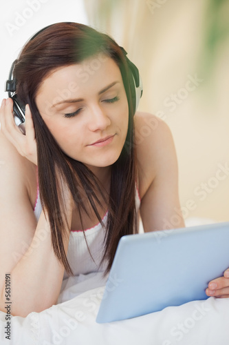 Relaxed girl listening to music and using a tablet pc lying on a