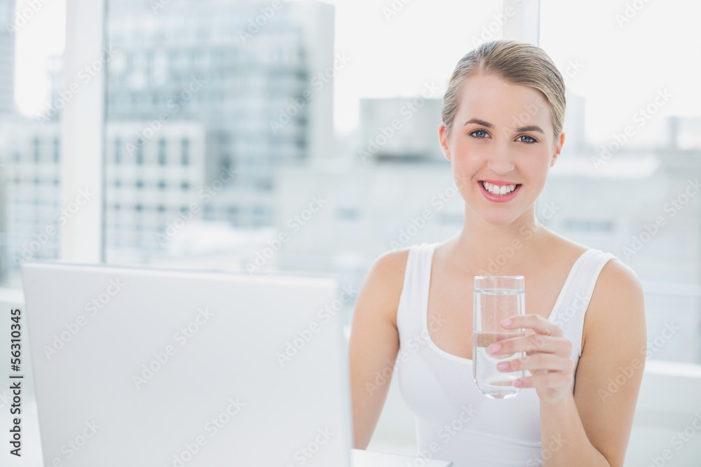 Pretty blonde holding glass of water using her laptop Pretty blonde holding glass of water using her laptop