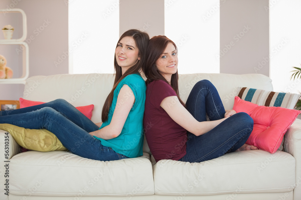 Two smiling friends sitting back to back on the sofa Two smiling friends sitting back to back on the sofa