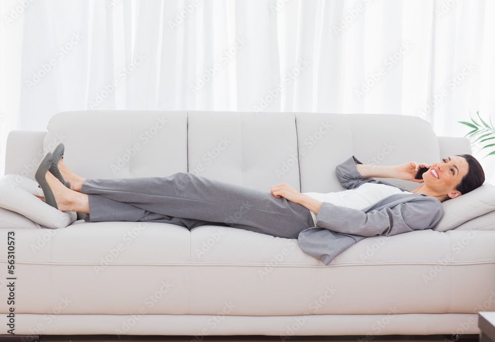 Businesswoman lying on sofa calling with her mobile phone