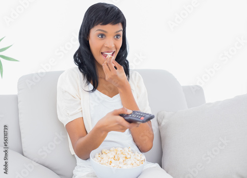Focused black haired woman in white clothes watching tv while ea