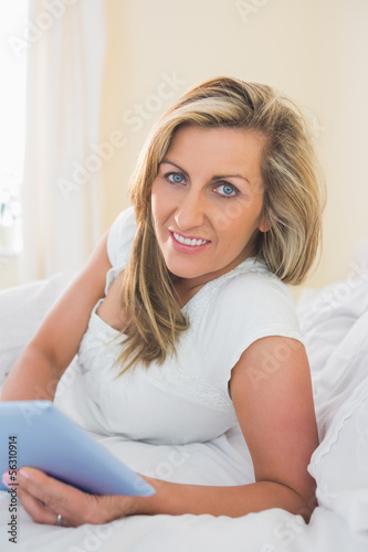 Pleased woman looking at camera using a tablet pc lying on her b Free Download Pleased woman looking at camera using a tablet pc lying on her b - GFXLoad