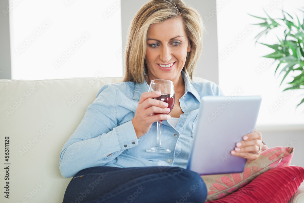 Smiling woman drinking wine and using a tablet pc Smiling woman drinking wine and using a tablet pc