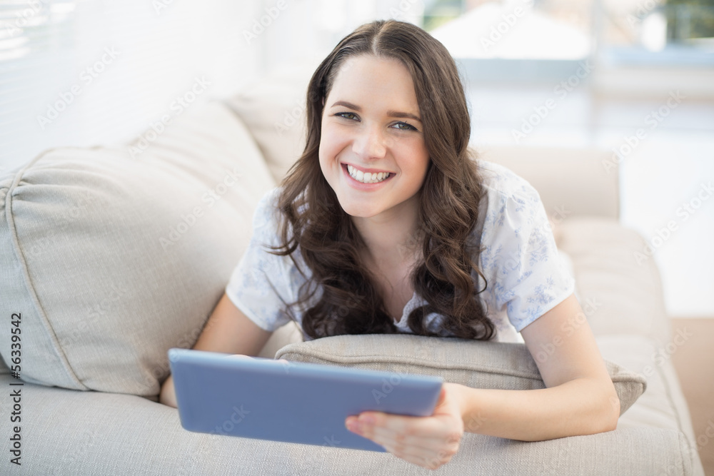 Cheerful woman lying on a cosy couch holding tablet pc Cheerful woman lying on a cosy couch holding tablet pc