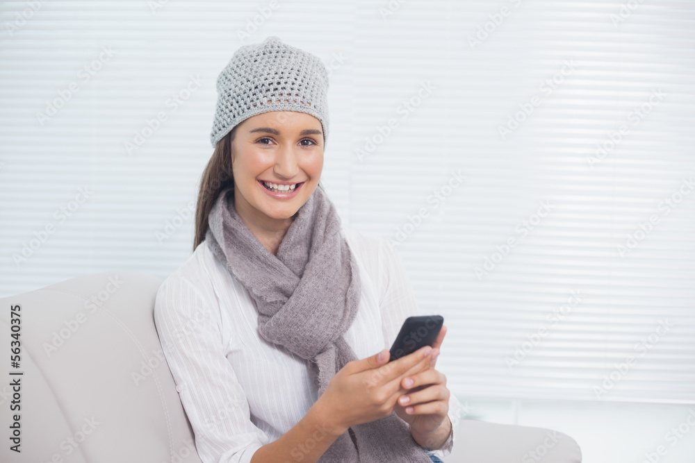 Cheerful pretty brunette with winter hat on holding her phone Cheerful pretty brunette with winter hat on holding her phone