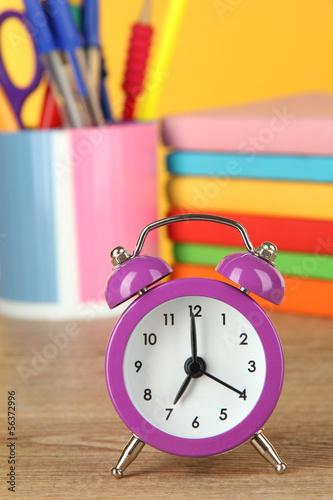 Purple alarm clock on table on yellow background