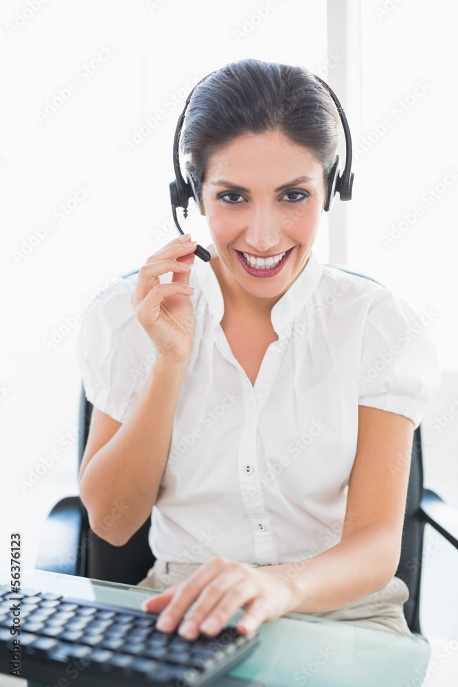 Smiling call centre agent working at her desk on a call Smiling call centre agent working at her desk on a call