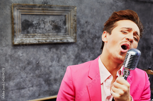 Young man in pink suit sings into microphone