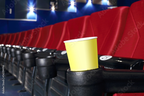 Yellow cup for popcorn is stand at red seat in auditorium