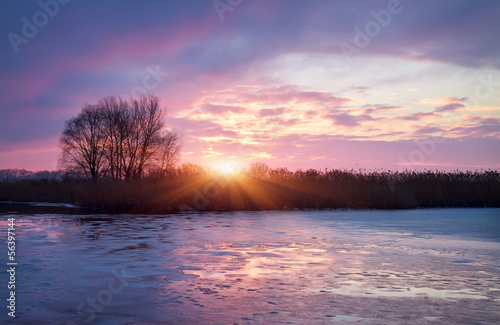 Winter landscape with sunrise sun and frozen river.