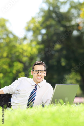 Happy businessman lying on a grass and working on laptop in park