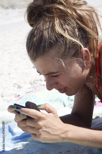 ragazza sulla spiaggia  invia messagi al telefono photo