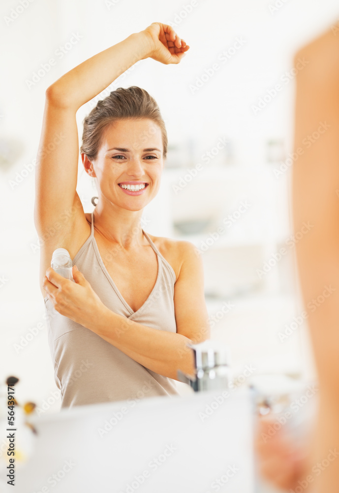Happy woman applying roller deodorant on underarm in bathroom Happy woman applying roller deodorant on underarm in bathroom