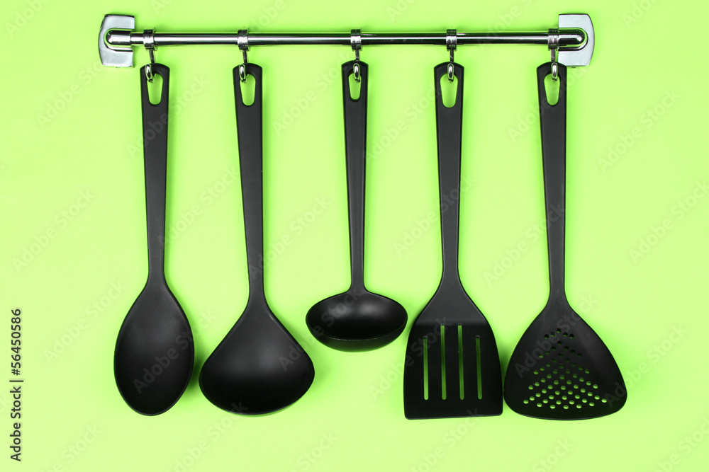 Black kitchen utensils on silver hooks, on green background Black kitchen utensils on silver hooks, on green background