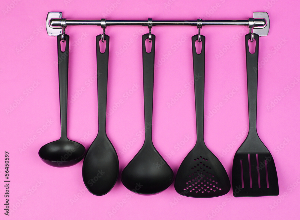 Black kitchen utensils on silver hooks, on pink background Black kitchen utensils on silver hooks, on pink background