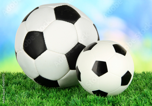 Soccer balls on green grass on bright background