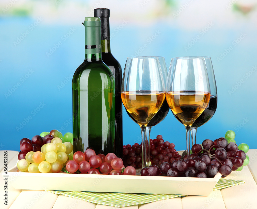 Wine bottles and glasses of wine on tray, on bright background