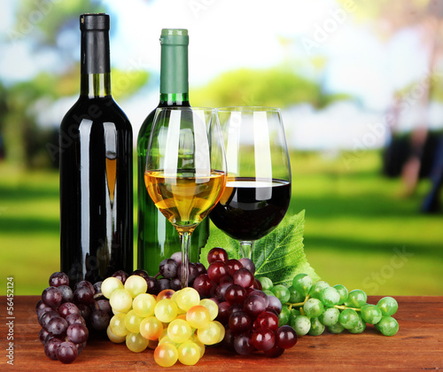 Wine bottles and glasses of wine on bright background
