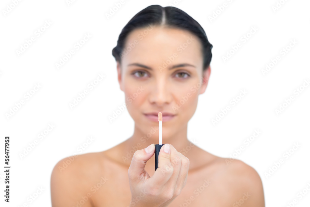 Young model holding lip gloss while looking at camera Young model holding lip gloss while looking at camera