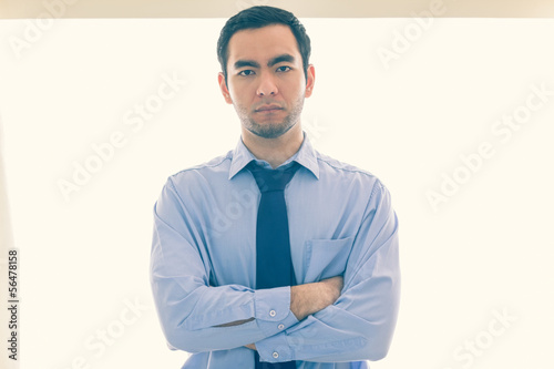 Serious man looking at camera standing in front of a window