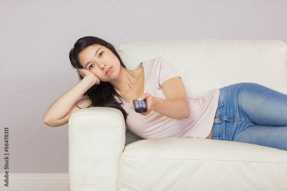 Bored asian girl lying on the couch watching tv Bored asian girl lying on the couch watching tv