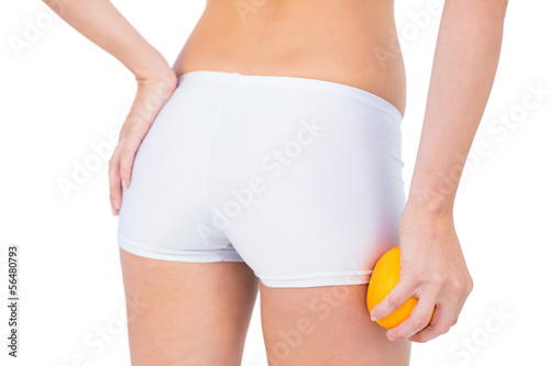 Rear view of fit woman holding orange by her thigh