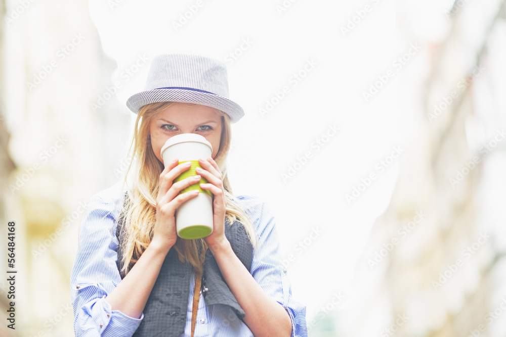 Hipster girl drinking hot beverage on city street