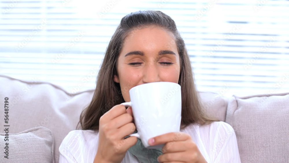 Smiling brunette sitting on sofa drinking her cup Smiling brunette sitting on sofa drinking her cup