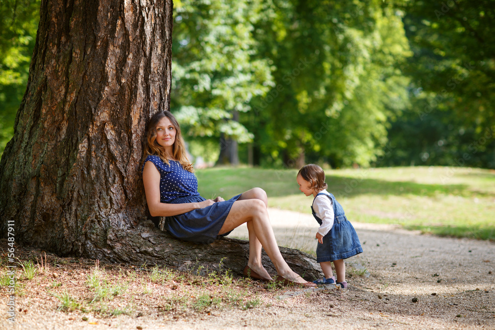 Fototapeta premium Beautiful mother and little daughter walking in summer park