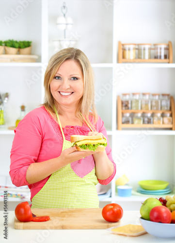 Happy smiling woman in kitchen preparing  sandwich