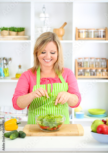 Happy smiling woman in kitchen preparing vegetable salad