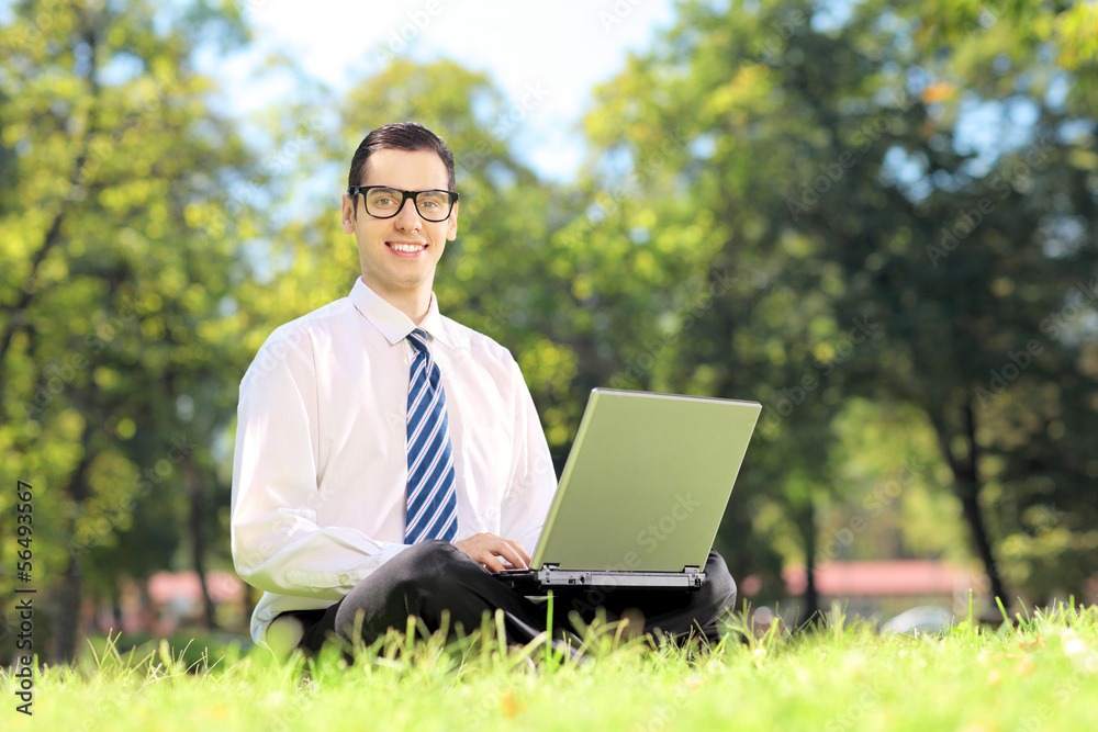 Man with glasses sitting on a grass and working on a laptop Man with glasses sitting on a grass and working on a laptop