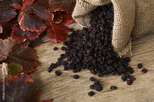 Black raisins in burlap bag over wooden table