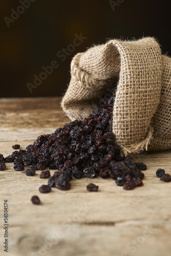 Black raisins in burlap bag over wooden table