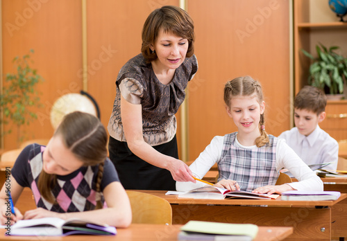 School kids work at lesson. Teacher controlling learning process